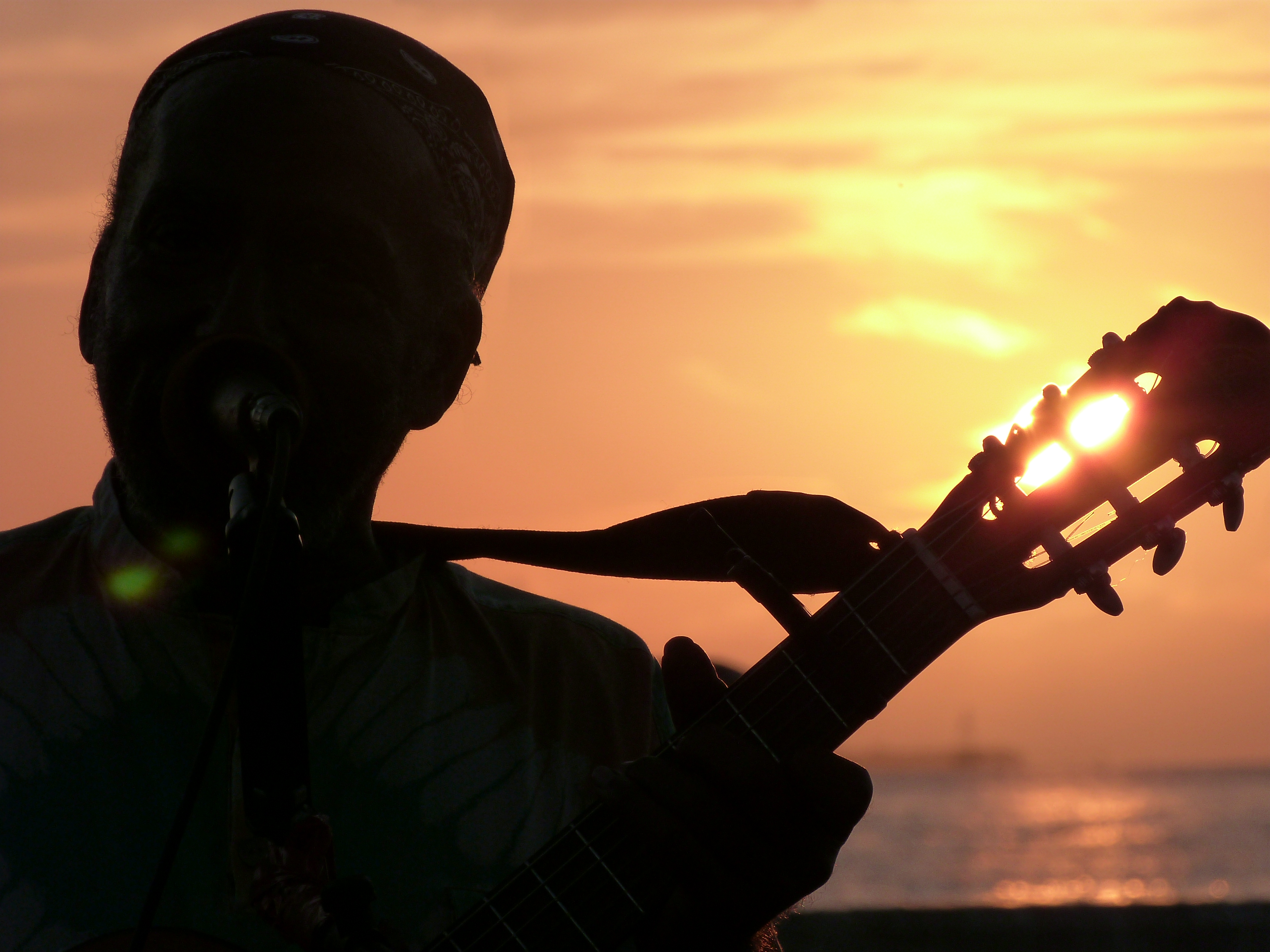 the sun is going down through a street performers guitar at mallory square in Key West Florida.