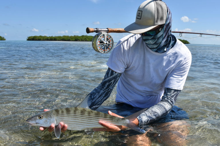 Nick Labadie is kneeling on a backcountry flat in a less than a foot of gin clear lower keys water holding a beautiful bonefish caught with a fly rod.