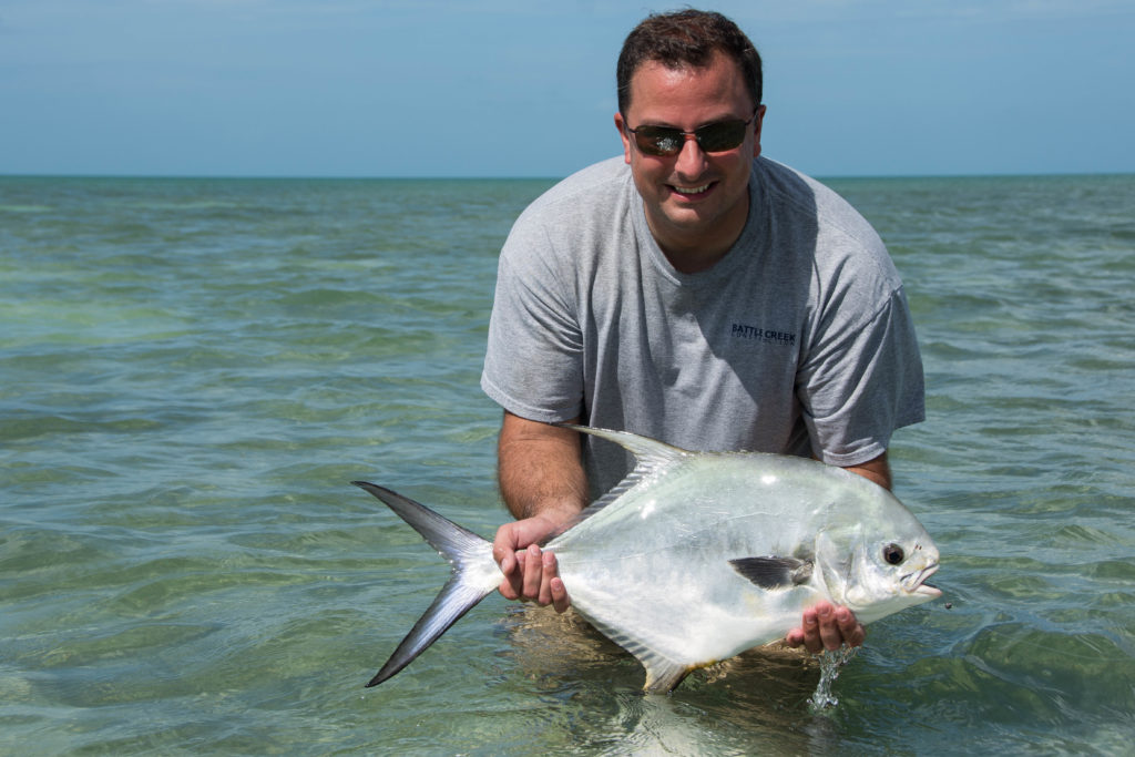 An angler is standing in the water holding a freshly caught permit off of the flats in in the Florida keys.